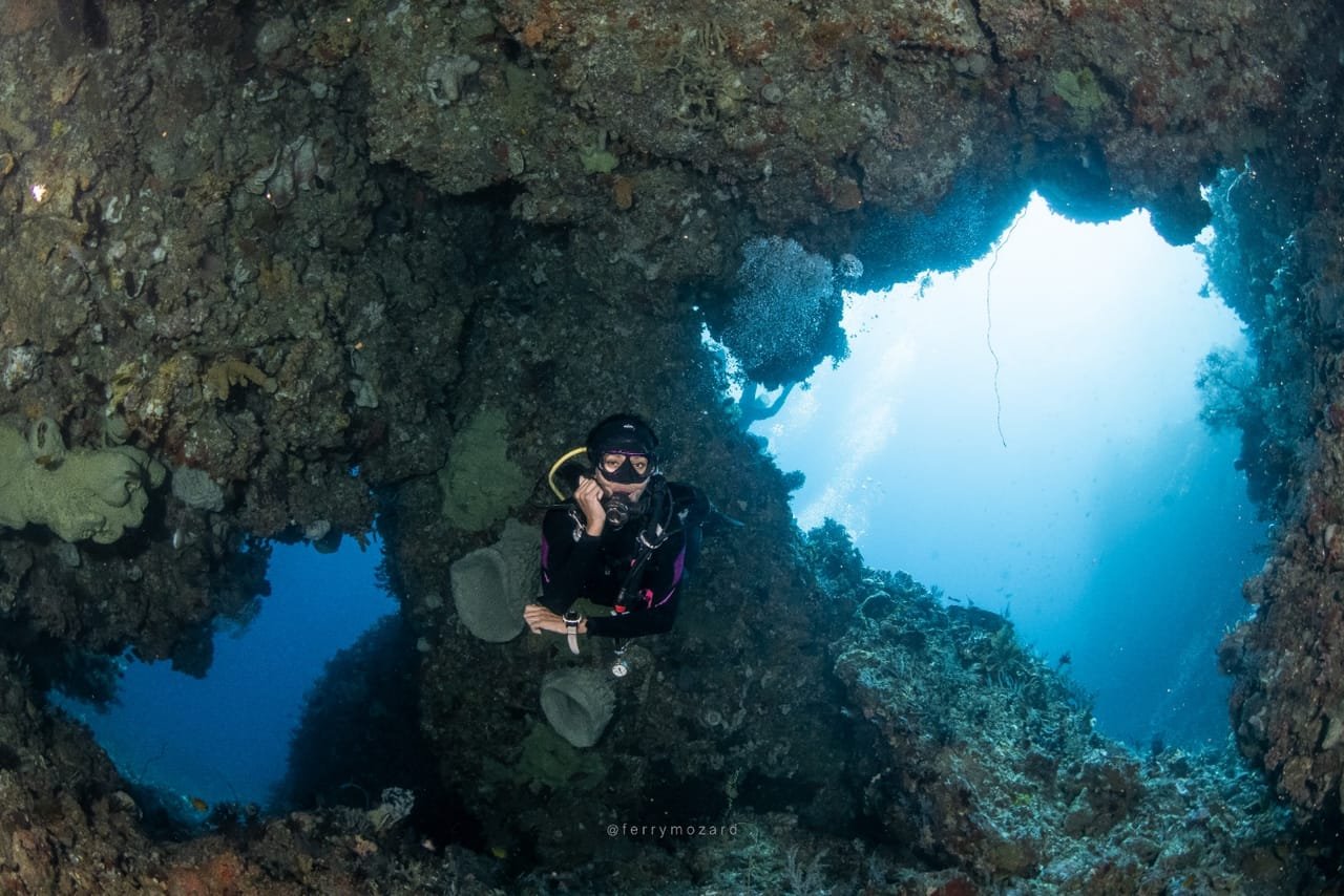 Diver framed by a coral swim-through with sunlight streaming through the opening