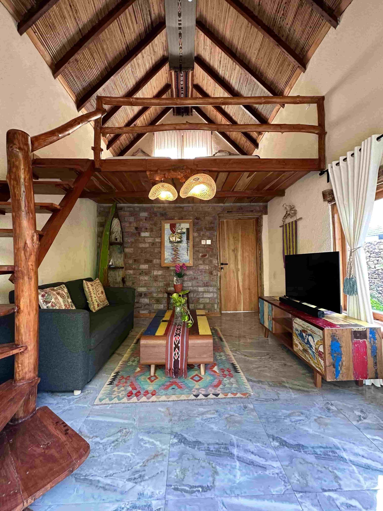 A-frame Loft Suite interior with thatched ceiling, mezzanine, and timber beams